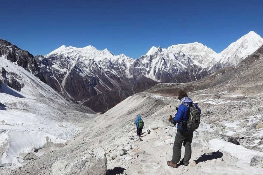 Trekker in blue jacket descending rocky slope with dramatic Himalayan mountain vista